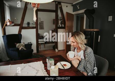 Donna al tavolo della colazione bere caffè Foto Stock