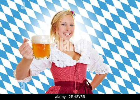 Giovane donna attraente a dirndl con birra di fronte alla bandiera bavarese Foto Stock