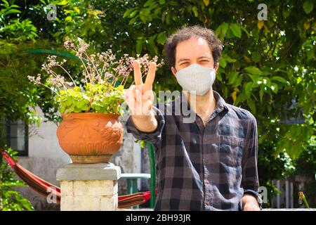 Giovane uomo con maschera di prevenzione facendo segno di vittoria Foto Stock