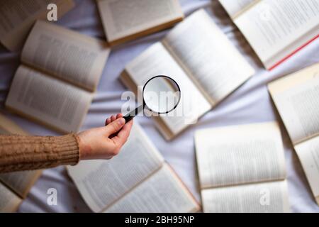 Mano con lente di ingrandimento su uno sfondo con libri. Foto Stock