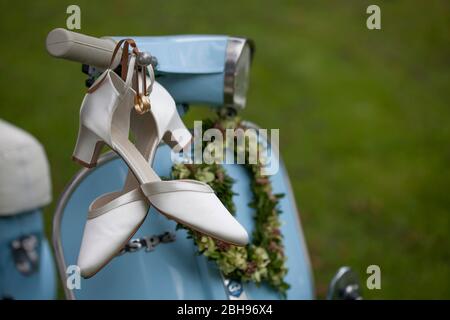 Anelli e scarpe da sposa appendono sul manubrio di una Vespa blu chiaro Foto Stock