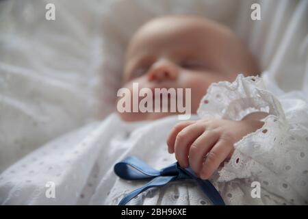 bambino di due mesi con un gown di battesimo sdraiato su cuscino bianco, Foto Stock