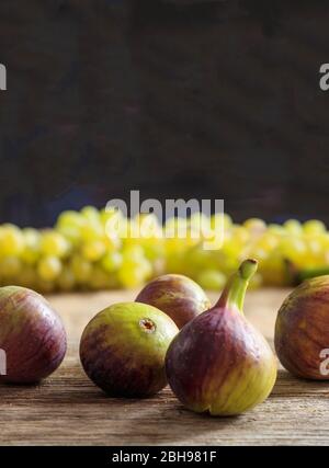 Fichi viola e uva verde sfocata su superficie in legno. Frutta fresca per la dieta, vegana, vegetariana, sfondo nero, concetto di stile di vita sano Foto Stock