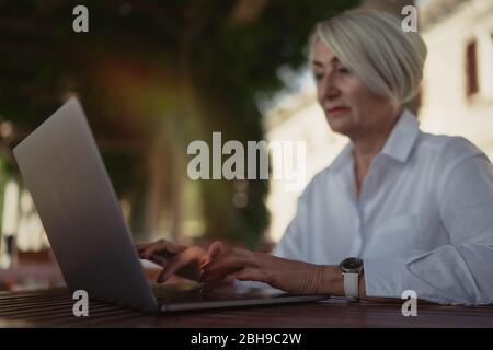 Donna senior sicura che digita il testo su un computer portatile in un bar Foto Stock