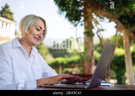 Donna senior sicura che digita il testo su un computer portatile in un bar Foto Stock