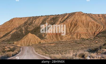 RoadTrip in inverno attraverso il semi-deserto Bardenas Reales, Navarra, Spagna. Riserva della Biosfera UNESCO con, tra gli altri, Castil de Tierra, i Monti Pisquerra e Bardena Blanca. Strada ghiaia. Foto Stock