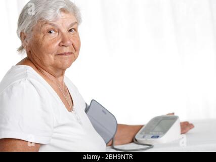 Donna anziana che misura la pressione sanguigna con manometro automatico Foto Stock