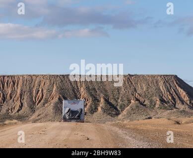 RoadTrip in inverno attraverso il semi-deserto Bardenas Reales, Navarra, Spagna. Riserva della Biosfera UNESCO con, tra gli altri, Castil de Tierra, i Monti Pisquerra e Bardena Blanca. Casa mobile su strada di ghiaia. Foto Stock