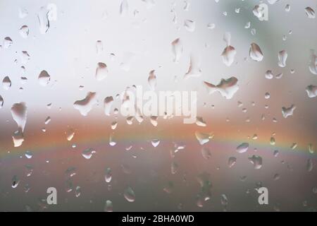 Le luci colorate di un arcobaleno dietro un vetro di finestra di pioggia con gocce di pioggia. Foto Stock