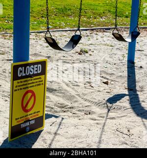 Un cartello avverte i visitatori di un parco locale che le strutture ricreative, come questo swing set per bambini, sono chiuse a causa del COVID-19. Foto Stock