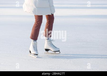 Primo piano di gambe donna in pantaloni rosso controllato su pattini su una pista di pattinaggio aperta, spazio copia. Giorno di sole. Sport invernali in città Foto Stock