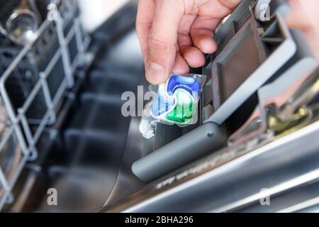 Primo piano della mano dell'uomo che mette la compressa in una scatola detergente per lavastoviglie, messa a fuoco morbida. Concetto di piatti sporchi. Foto Stock