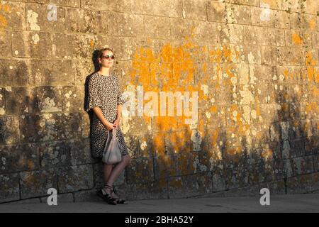 Donna appoggiata contro il muro di ipercrescita al sole della sera Foto Stock