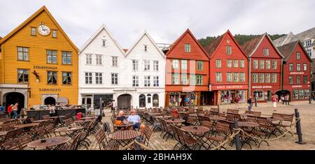 I turisti siedono ai tavoli sullo sfondo storico di case di legno colorate a Bryggen nel quartiere anseatico di Bryggen, Torget, il Molo Tedesco, Bergen, Hordaland, Norvegia, Scandinavia, Europa Foto Stock