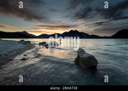 Pietre e sullo sfondo Steinmandl sulla riva di Walchensee durante il tramonto. Sullo sfondo le Prealpi bavaresi con l'Herzogstand, Heimgarten e Simetsberg. Foto Stock