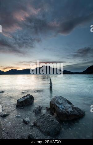 Pietre e sullo sfondo Steinmandl sulla riva di Walchensee durante il tramonto. Sullo sfondo le Prealpi bavaresi con l'Herzogstand, Heimgarten e Simetsberg. Foto Stock