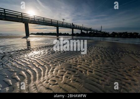 Ostsee im strahlenden Gegenlicht mit der Seebrücke in Wustrow und Spiegelung der schönen Wolken am Strand Foto Stock