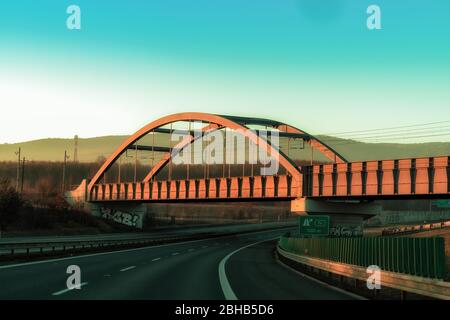 Ponte ferroviario color rame su un'autostrada in un vivace tramonto Foto Stock