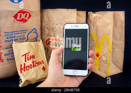 Calgary, Alberta. Canada. 24 aprile 2020: Una persona che detiene un iPhone Plus con l'applicazione Uber Eats aperta con le confezioni di cibo fornite da Tim Hourto Foto Stock