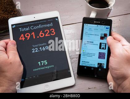 L'uomo tiene la tavoletta in mano con la statistica aggiornata Coronavirus COVID-19 live e in altra mano smartphone con le notizie sul tavolo con caffè, Messico, nel marzo 26, 2020 Foto Stock