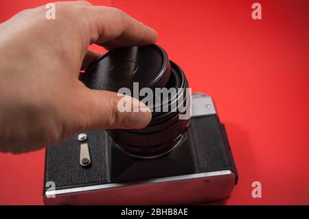 Vecchia fotocamera retro sovietico Zenit-e in mano. Fotocamera reflex d'epoca anni '80 del 20 ° secolo in ex URSS su un backgrounde rosso Foto Stock