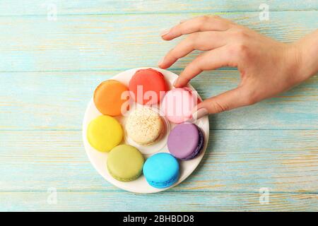 Femmina mano prendendo gustosi macaroon colorati da piccolo piatto su sfondo di legno colore Foto Stock