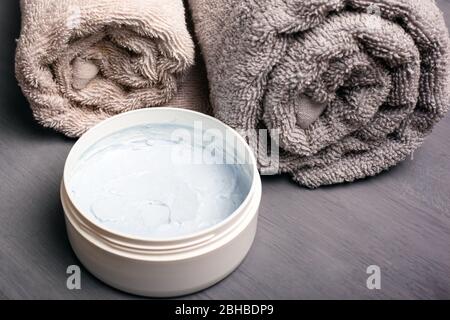 asciugamani in rotolo color pastello e scrub corpo su sfondo grigio primo piano. cosmetici per il corpo, accessori per il bagno. Foto Stock