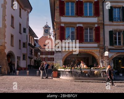 Strada acciottolata e splendidi edifici della città vecchia di Murten in una giornata di sole. La gente si gode il pomeriggio sulla terrazza di una sala da tè. Foto Stock