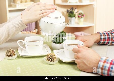 Mani femminili e maschili con tazze di tè, primo piano, sullo sfondo interno della casa Foto Stock