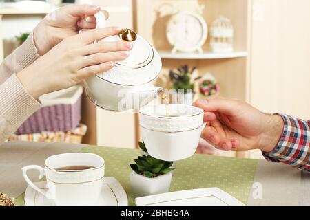 Mani femminili e maschili con tazze di tè, primo piano, sullo sfondo interno della casa Foto Stock