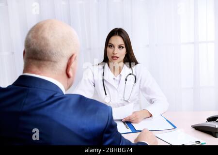 Giovane medico femminile che riceve paziente nel suo ufficio su sfondo bianco tenda Foto Stock