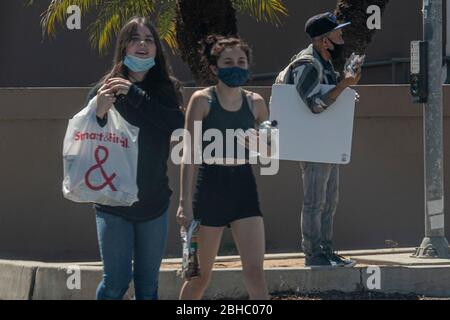 Los Angeles, California, Stati Uniti. 24 Aprile 2020. Due ragazze lasciano un negozio DI alimentari INTELLIGENTE E FINALE mentre un uomo vende maschere in un angolo di strada, mentre la gente va circa la vita quotidiana sotto le restrizioni COVID-19 a Los Angeles, California, il Venerdì, Aprile 24. Foto di Justin L. Stewart Credit: Justin L. Stewart/ZUMA Wire/Alamy Live News Foto Stock