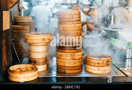 Pile di stufatori di bambù impilati sono fumanti per dim sum di fronte al ristorante con chef sfocati sullo sfondo a Taipei, Taiwan. Foto Stock