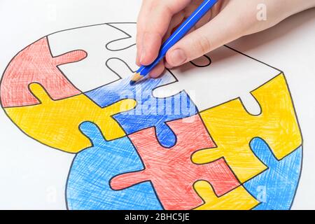 Giornata mondiale di consapevolezza autistica. La mano dei bambini trae il cuore dai puzzle multicolore. Concetto di salute mentale. Foto Stock