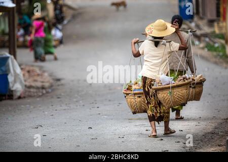 Donne birmane che trasportano il cibo con un metodo tipico. Abiti con caratteristico cappello del luogo. Sulla strada con spazio copia a sinistra. Posizione: Foto Stock