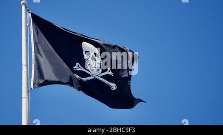 Cranio e crossoni bandiera pirata nera che vola, conosciuta anche come Jolly Roger, simboleggia veleno, morte, pericolo e tradimento. Visto sulle navi pirata. Foto Stock