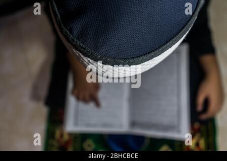 Makassar, Sulawesi del Sud, Indonesia. 25 Aprile 2020. Un ragazzo sta leggendo il Corano seriamente nella sua stanza durante Ramadan mentre aspetta il Breaking the Fast a Makassar, nella provincia di Sulawesi del Sud, Indonesia. Nel mese del Ramadan, ogni musulmano effettua il digiuno ed anche l'altro culto come la lettura del Corano e fare il dhikr per riempire il tempo libero, particolarmente durante l'epidemia di Covid-19. Credit: Herwin Bahar/ZUMA Wire/Alamy Live News Foto Stock