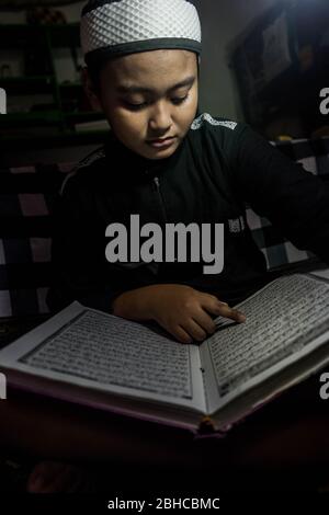 Makassar, Sulawesi del Sud, Indonesia. 25 Aprile 2020. Un ragazzo sta leggendo il Corano seriamente nella sua stanza durante Ramadan mentre aspetta il Breaking the Fast a Makassar, nella provincia di Sulawesi del Sud, Indonesia. Nel mese del Ramadan, ogni musulmano effettua il digiuno ed anche l'altro culto come la lettura del Corano e fare il dhikr per riempire il tempo libero, particolarmente durante l'epidemia di Covid-19. Credit: Herwin Bahar/ZUMA Wire/Alamy Live News Foto Stock