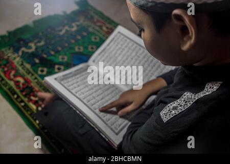 Makassar, Sulawesi del Sud, Indonesia. 25 Aprile 2020. Un ragazzo sta leggendo il Corano seriamente nella sua stanza durante Ramadan mentre aspetta il Breaking the Fast a Makassar, nella provincia di Sulawesi del Sud, Indonesia. Nel mese del Ramadan, ogni musulmano effettua il digiuno ed anche l'altro culto come la lettura del Corano e fare il dhikr per riempire il tempo libero, particolarmente durante l'epidemia di Covid-19. Credit: Herwin Bahar/ZUMA Wire/Alamy Live News Foto Stock