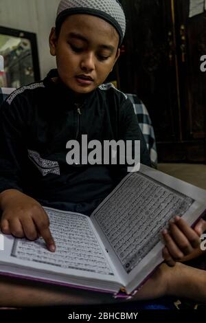 Makassar, Sulawesi del Sud, Indonesia. 25 Aprile 2020. Un ragazzo sta leggendo il Corano seriamente nella sua stanza durante Ramadan mentre aspetta il Breaking the Fast a Makassar, nella provincia di Sulawesi del Sud, Indonesia. Nel mese del Ramadan, ogni musulmano effettua il digiuno ed anche l'altro culto come la lettura del Corano e fare il dhikr per riempire il tempo libero, particolarmente durante l'epidemia di Covid-19. Credit: Herwin Bahar/ZUMA Wire/Alamy Live News Foto Stock