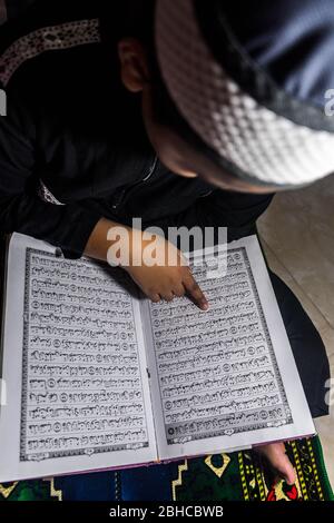 Makassar, Sulawesi del Sud, Indonesia. 25 Aprile 2020. Un ragazzo sta leggendo il Corano seriamente nella sua stanza durante Ramadan mentre aspetta il Breaking the Fast a Makassar, nella provincia di Sulawesi del Sud, Indonesia. Nel mese del Ramadan, ogni musulmano effettua il digiuno ed anche l'altro culto come la lettura del Corano e fare il dhikr per riempire il tempo libero, particolarmente durante l'epidemia di Covid-19. Credit: Herwin Bahar/ZUMA Wire/Alamy Live News Foto Stock