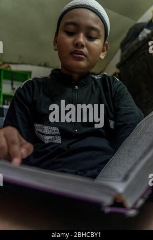 Makassar, Sulawesi del Sud, Indonesia. 25 Aprile 2020. Un ragazzo sta leggendo il Corano seriamente nella sua stanza durante Ramadan mentre aspetta il Breaking the Fast a Makassar, nella provincia di Sulawesi del Sud, Indonesia. Nel mese del Ramadan, ogni musulmano effettua il digiuno ed anche l'altro culto come la lettura del Corano e fare il dhikr per riempire il tempo libero, particolarmente durante l'epidemia di Covid-19. Credit: Herwin Bahar/ZUMA Wire/Alamy Live News Foto Stock