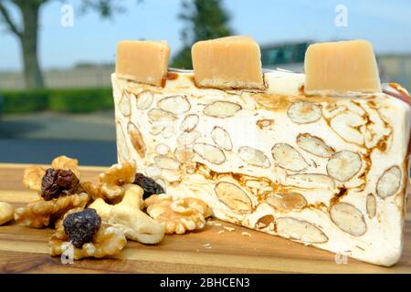 Delizioso tradizionale grande pezzo italiano o torrone con noci, noci in primo piano su un asse di legno. Fuoco selettivo. Albero in backkground Foto Stock