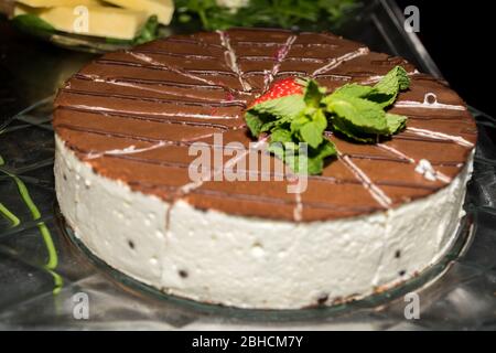 Torta intera rotonda a fette con fragola sulla parte superiore e frutta, su un piatto di vetro semplice table.Hote ricetta francese per dolce dolce dolce dolce, foglie di menta, Foto Stock