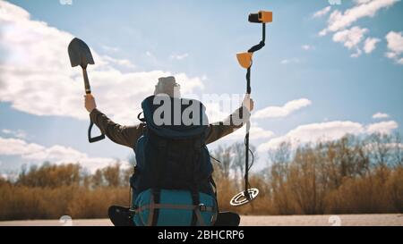 Donna con la pala e zaino alla ricerca di sabbia con il metal detector. Caccia al tesoro sulla spiaggia di andy. Foto Stock