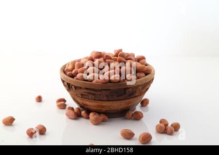 Arachidi o arachis crudi in una ciotola di legno su sfondo bianco Foto Stock