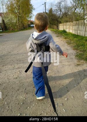 bambino di 2 anni con il guinzaglio. Il bambino che indossa l'imbracatura corre sul percorso Foto Stock