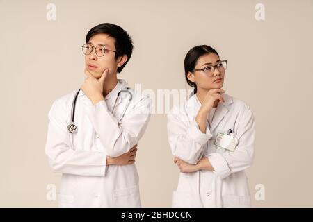 Immagine dei giovani medici asiatici in bianco uniforme pensiero sul problema di salute isolato su sfondo beige Foto Stock