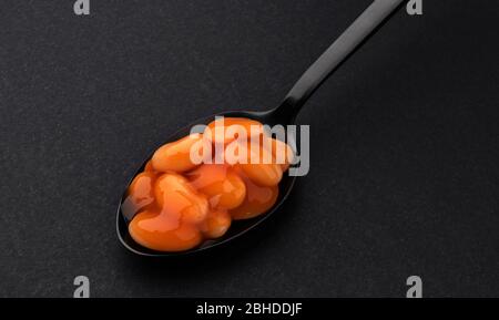 Cucchiaio di fagioli cotti in salsa di pomodoro isolato su fondo nero Foto Stock