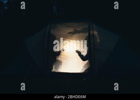 Silhouette di bambini che giocano in tenda da campeggio di notte facendo pupazzi d'ombra con torcia godendo vacanze estive Foto Stock